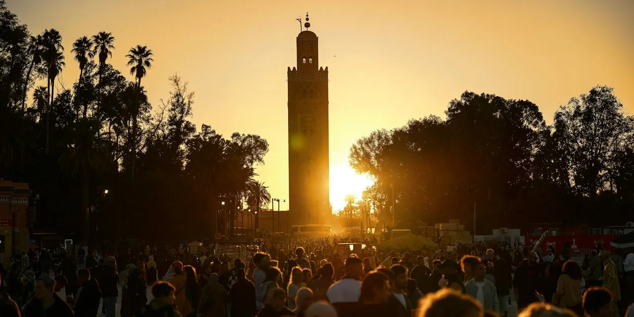 A bustling crowd gathers under the iconic Koutoubia Mosque tower at sunset in Marrakesh, Morocco.