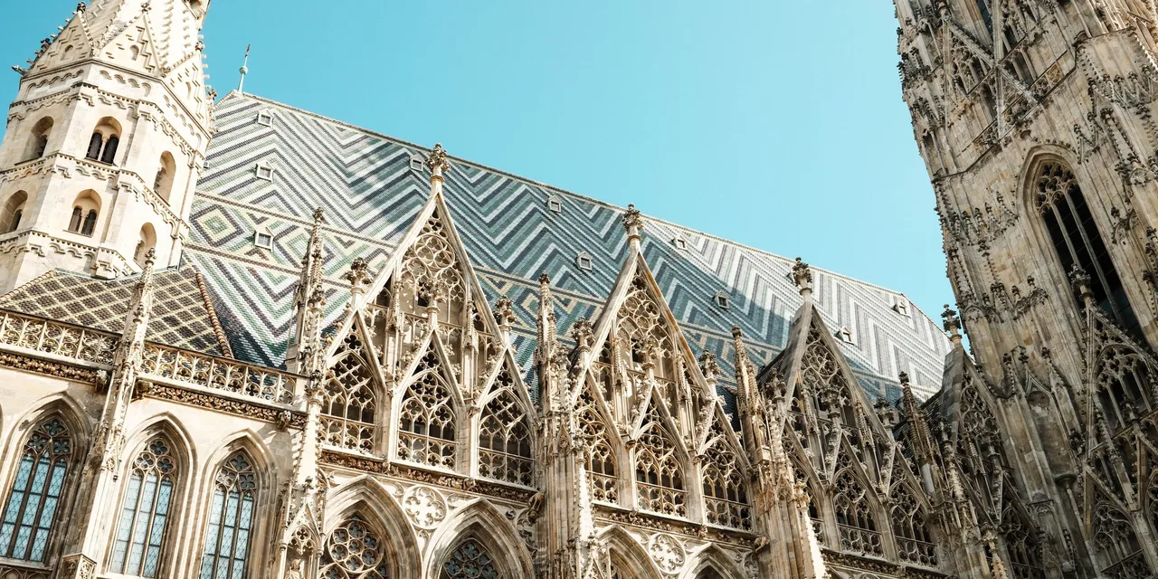 The patterned tiled roof and Gothic stonework of St Stephen's Cathedral in Vienna against a clear sky.