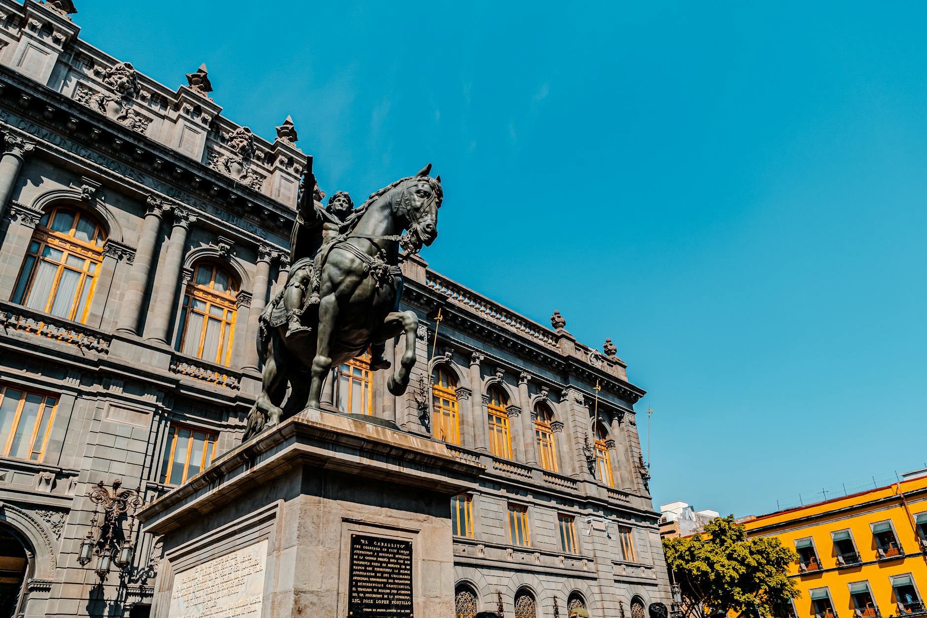 Low-angle shot of a historic building and statue in Mexico City with a clear blue sky.