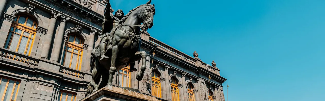 Low-angle shot of a historic building and statue in Mexico City with a clear blue sky.