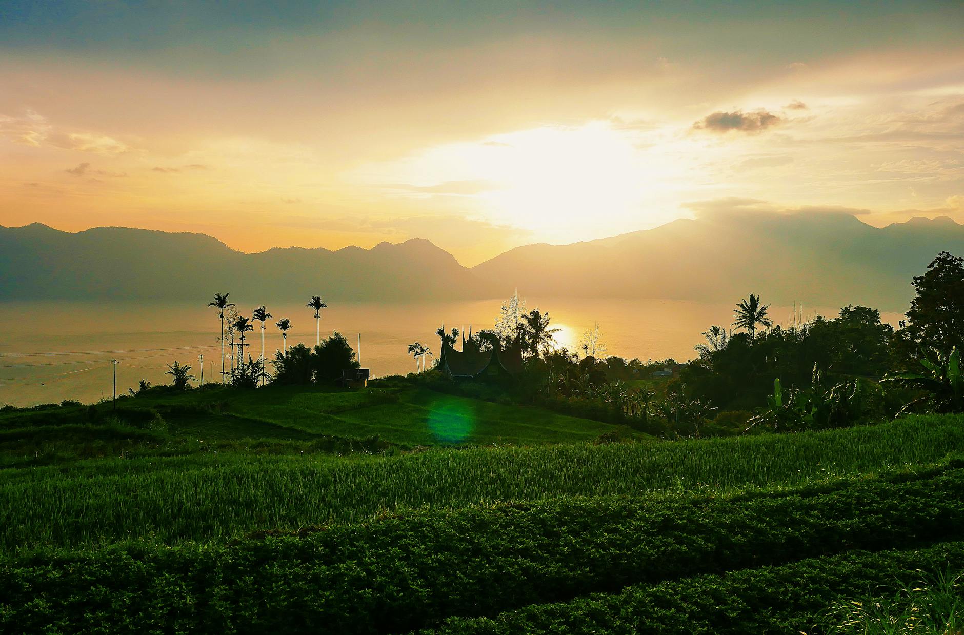 Peaceful landscape in West Sumatra, capturing a vibrant sunset over fields and mountains.