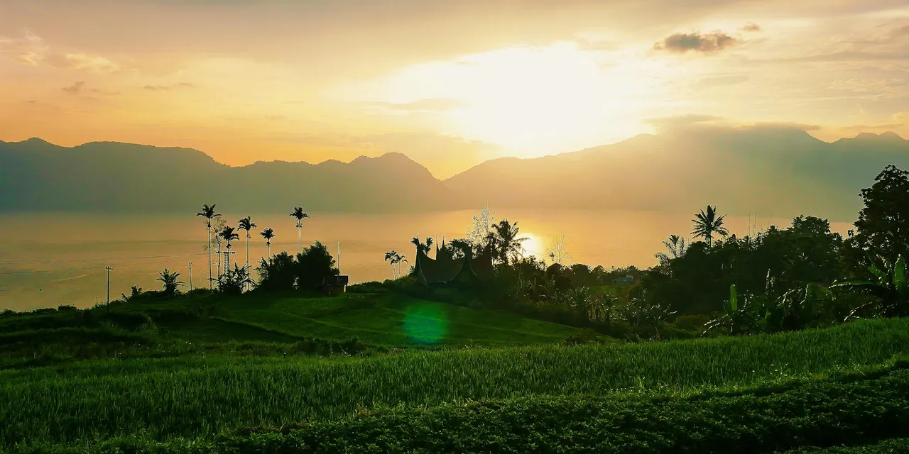 Peaceful landscape in West Sumatra, capturing a vibrant sunset over fields and mountains.