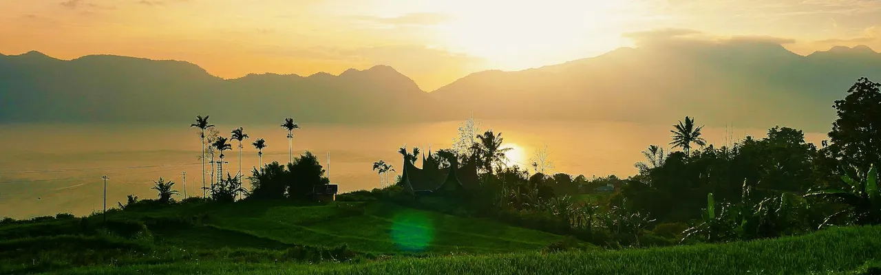 Peaceful landscape in West Sumatra, capturing a vibrant sunset over fields and mountains.