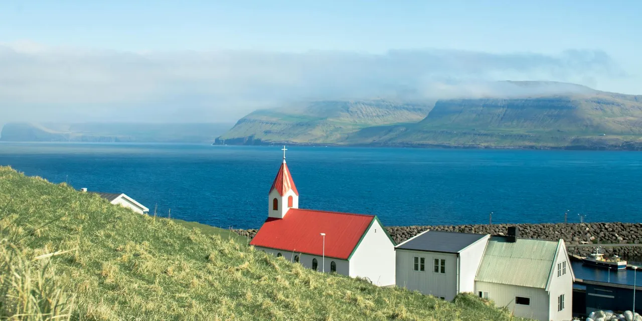 Idyllic coastal village view in Faroe Islands with traditional church and ocean backdrop.