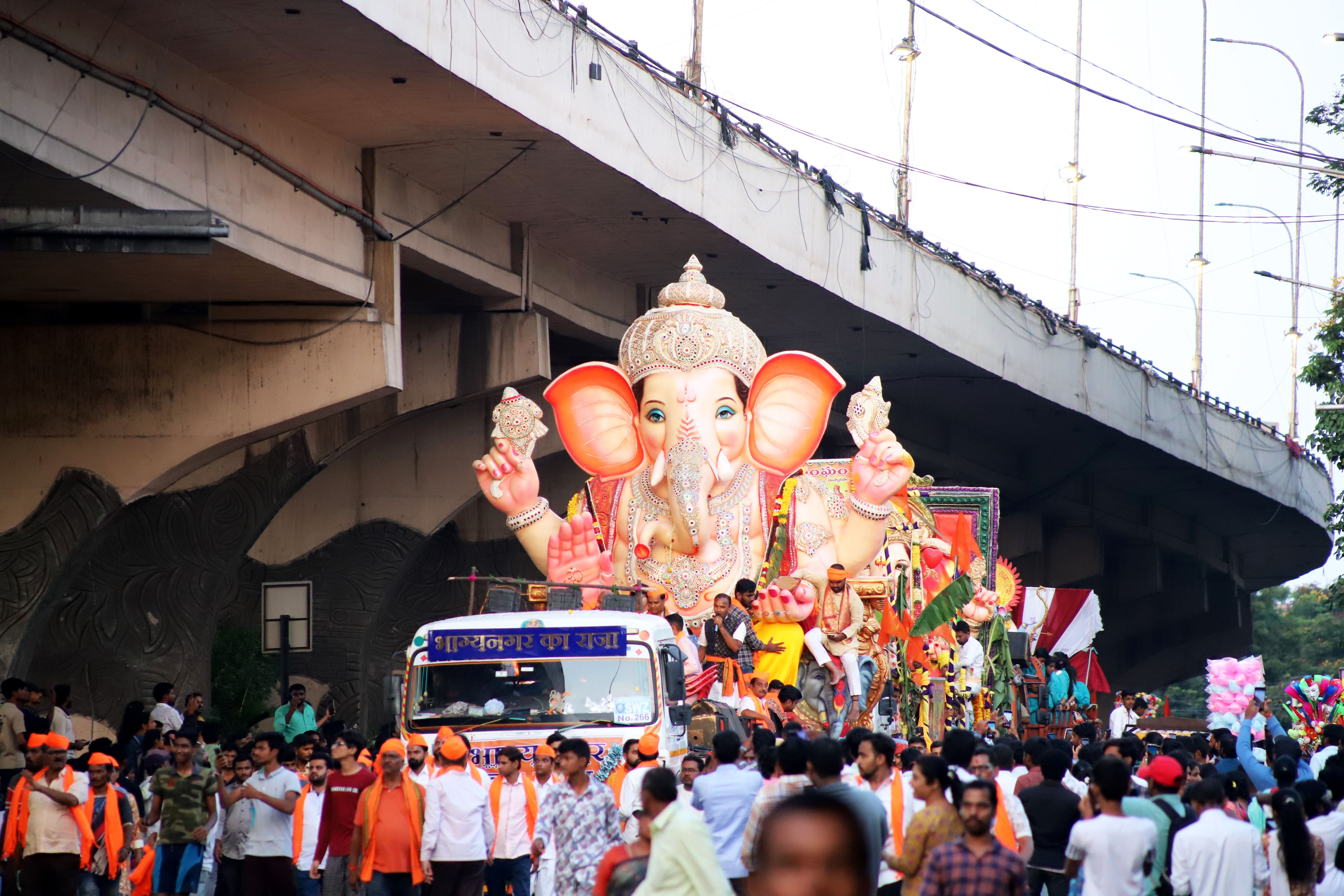 A large decorated Ganesha idol carried on a truck through a crowded Mumbai street during a festival procession.
