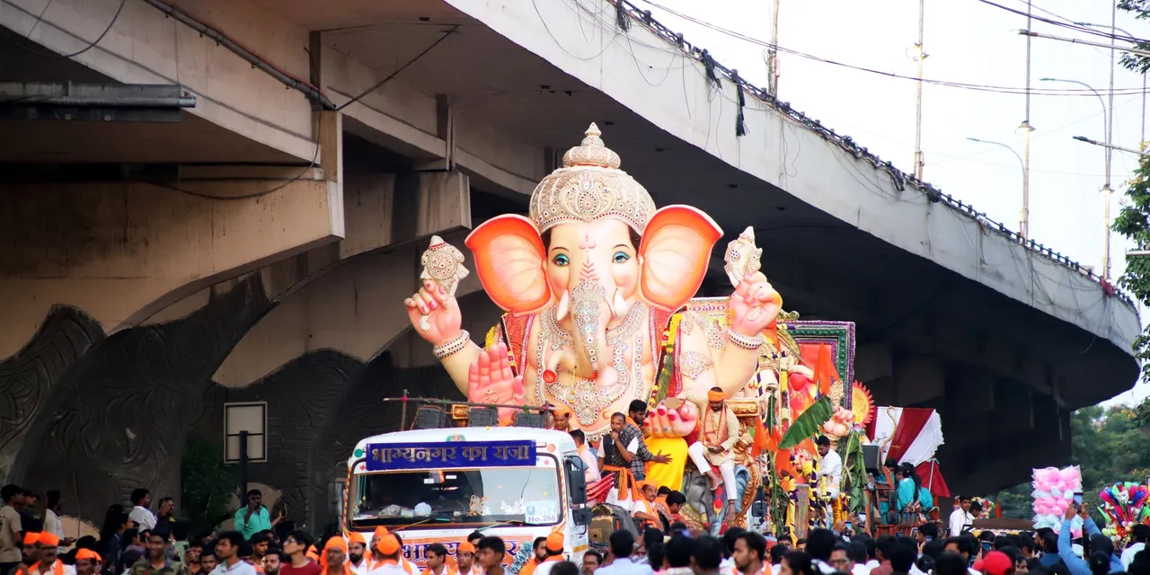 A large decorated Ganesha idol carried on a truck through a crowded Mumbai street during a festival procession.