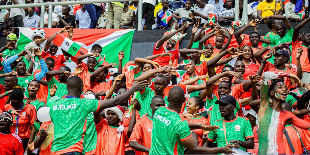 Colorful crowd with Burundi flags cheering enthusiastically at a sports event.