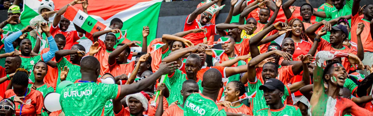 Colorful crowd with Burundi flags cheering enthusiastically at a sports event.