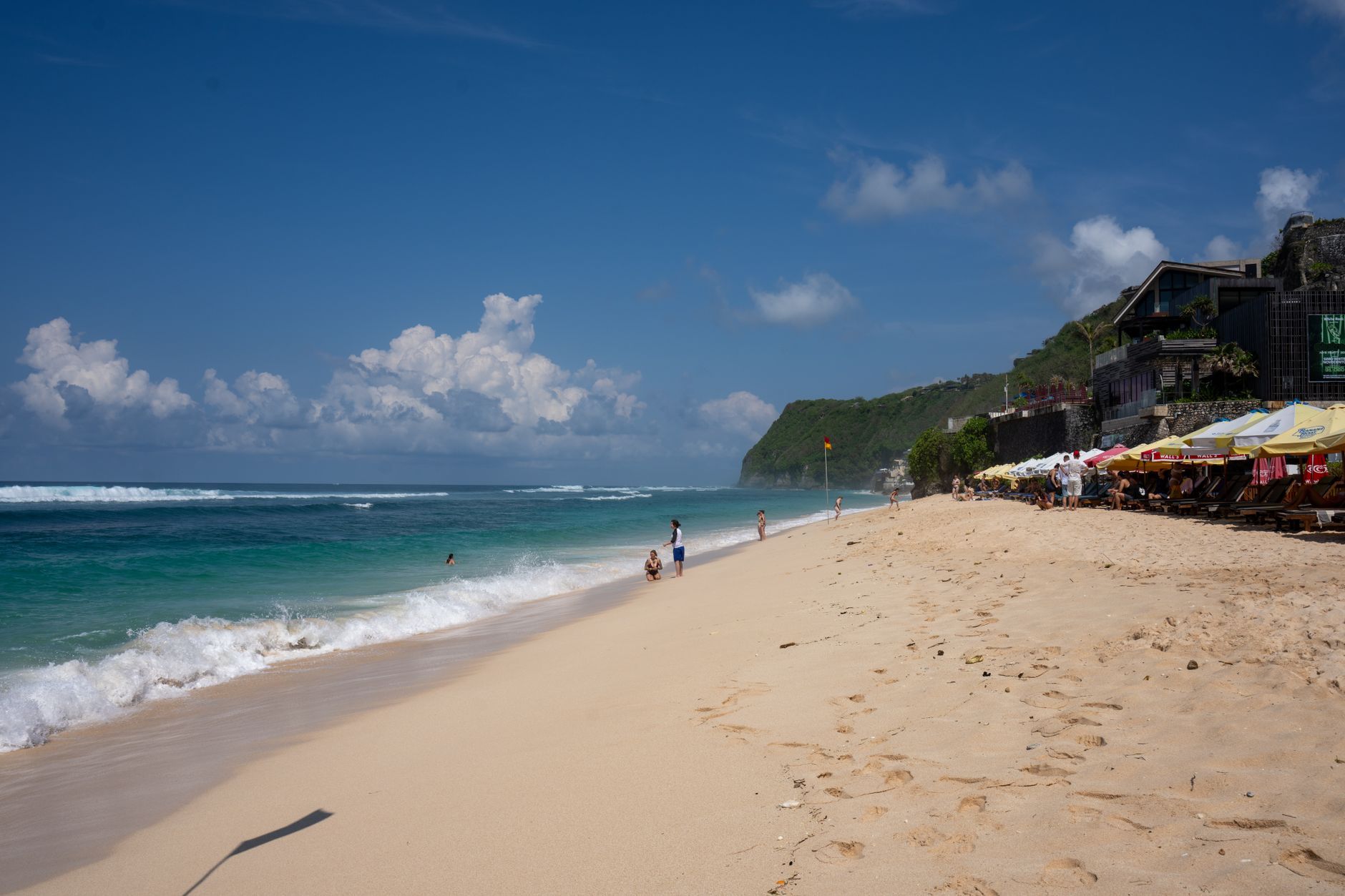 A vibrant beach scene in Bali, Indonesia with clear blue skies, ocean waves, and beachgoers enjoying the sun.