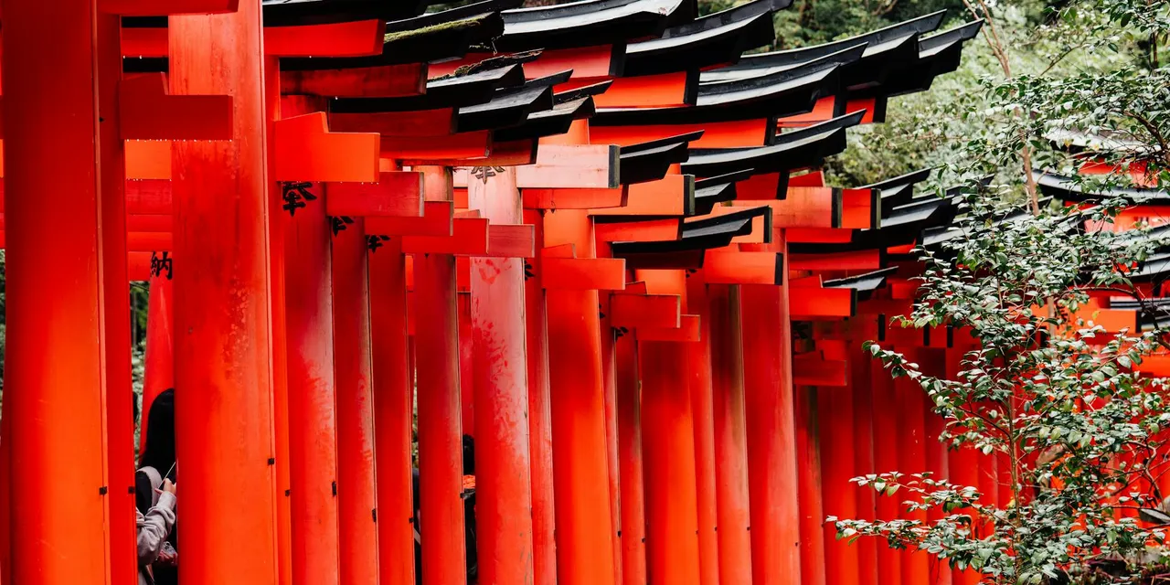 Explore the vibrant red torii gates at Fushimi Inari Shrine in Kyoto, Japan, surrounded by lush greenery.