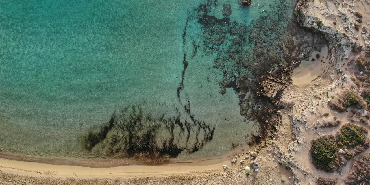 A stunning aerial photograph of Arenella Beach with turquoise waters and rocky shore in Sicily, Italy.
