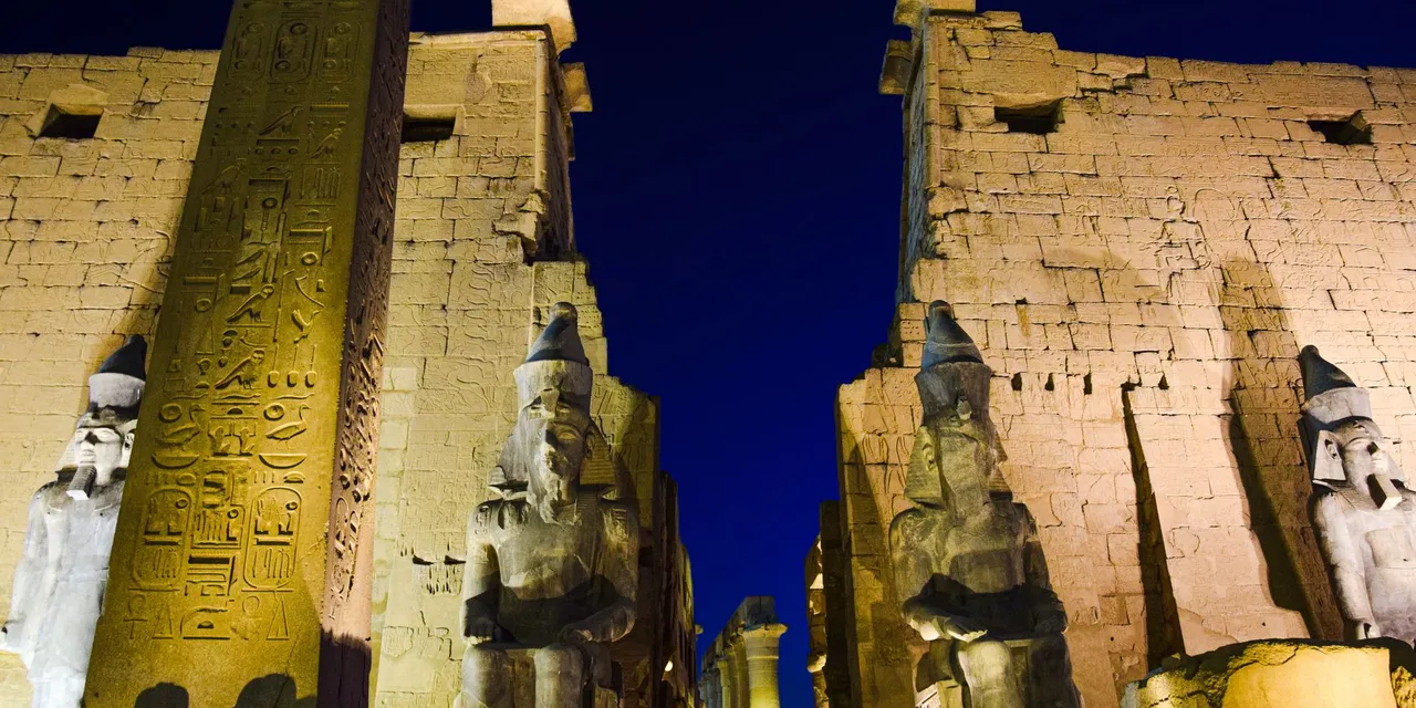 Night view of the illuminated Luxor Temple with ancient statues and hieroglyphs.