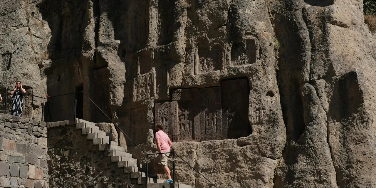 Visitors exploring the ancient rock-hewn carvings at Geghard Monastery Armenia.