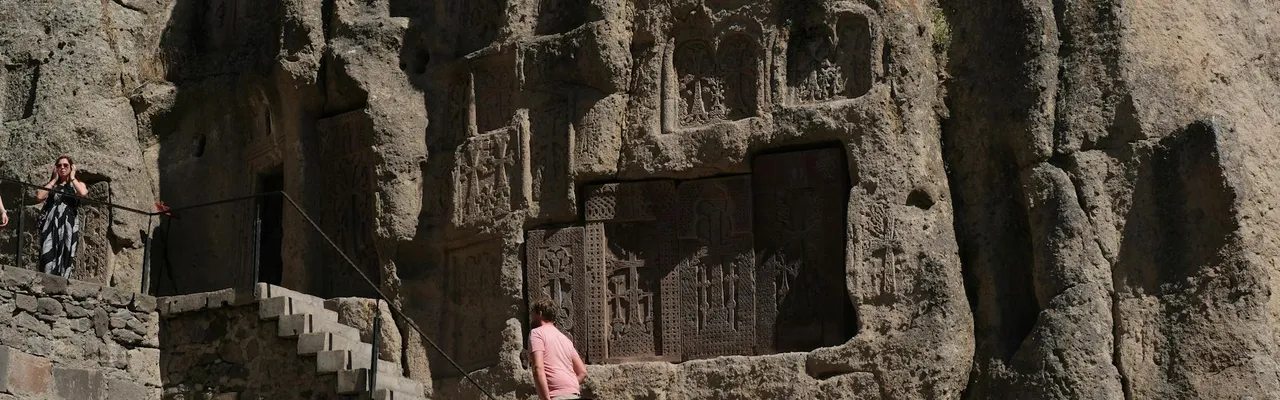 Visitors exploring the ancient rock-hewn carvings at Geghard Monastery Armenia.
