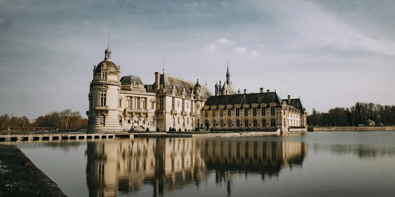 Stunning view of Château de Chantilly with reflection in a serene lake under a clear sky in France.