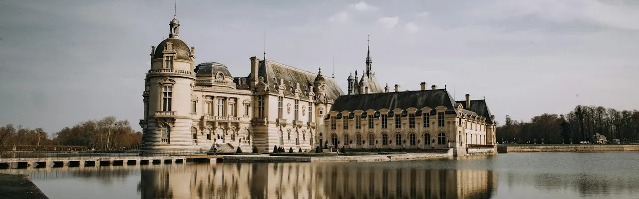 Stunning view of Château de Chantilly with reflection in a serene lake under a clear sky in France.