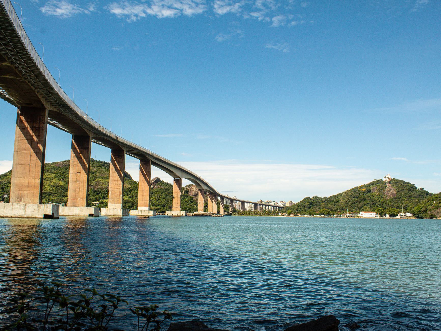 A stunning view of the Third Bridge in Vitória, Brazil against a clear blue sky and ocean.