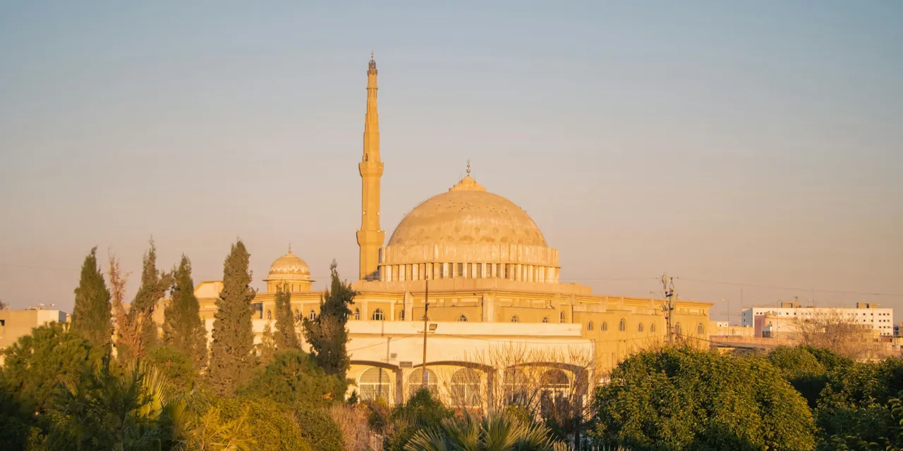 A sunlit mosque in Erbil, Kurdistan Region, Iraq, surrounded by trees.