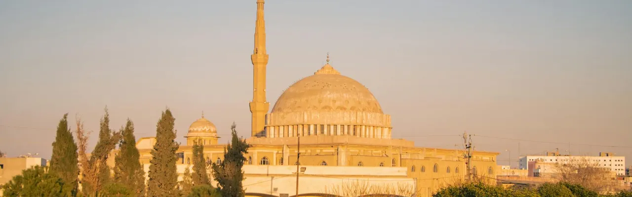 A sunlit mosque in Erbil, Kurdistan Region, Iraq, surrounded by trees.