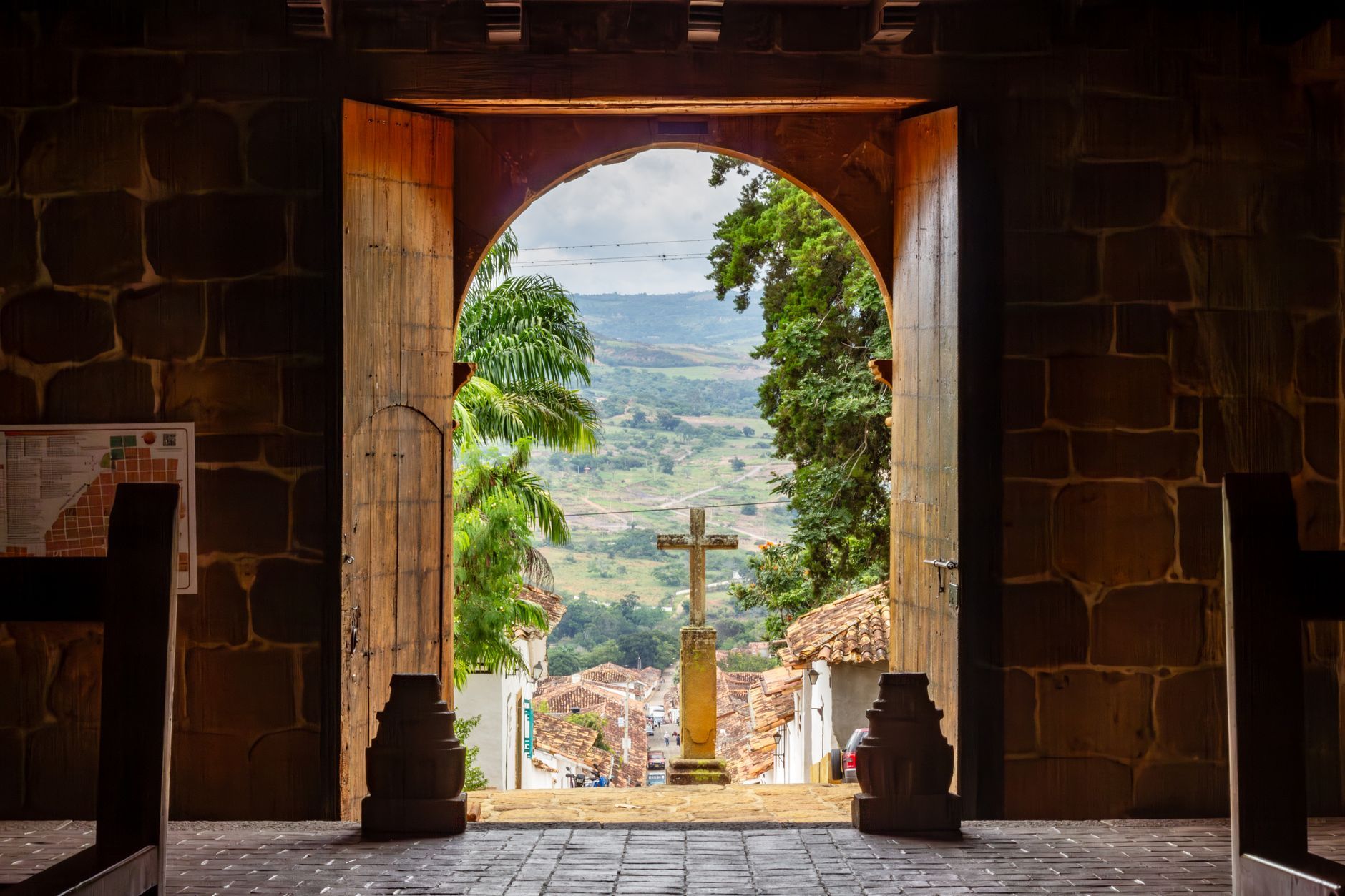View through a church entrance in Barichara, Colombia, with a stone cross outdoors.