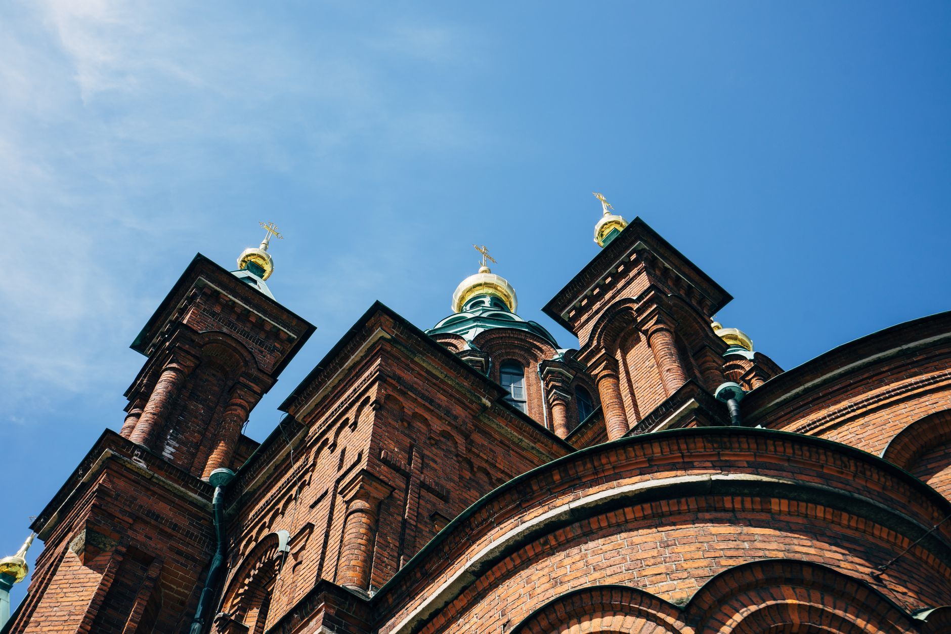 A low-angle view capturing the gold-domed architecture of Helsinki's iconic Orthodox Cathedral under a blue sky.