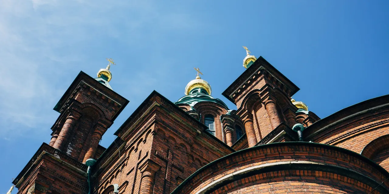 A low-angle view capturing the gold-domed architecture of Helsinki's iconic Orthodox Cathedral under a blue sky.