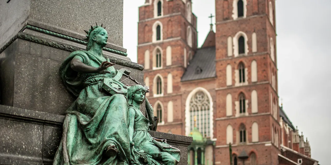 Bronze statue at Krakow Main Square with St Mary's Basilica rising behind, Poland
