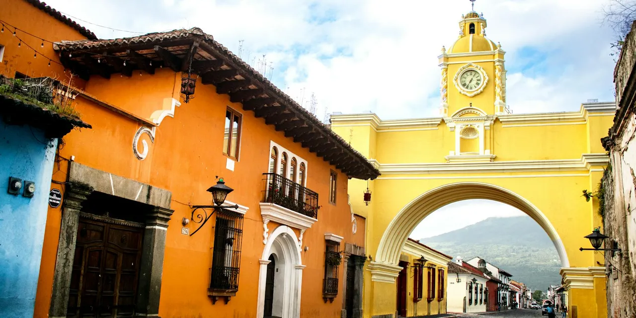 Colorful street with Santa Catalina Arch in Antigua, Guatemala. Vibrant colonial architecture and scenic mountainous backdrop.