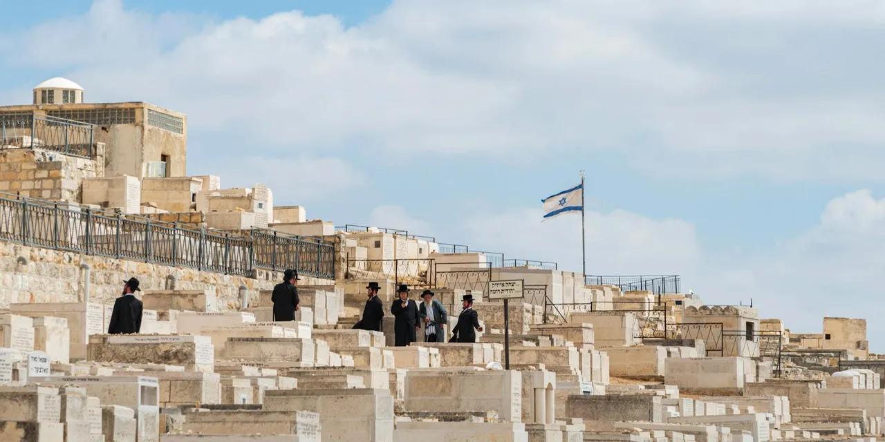 Orthodox Jewish men gather at Mount of Olives Cemetery in Jerusalem, Israel, under a clear sky.