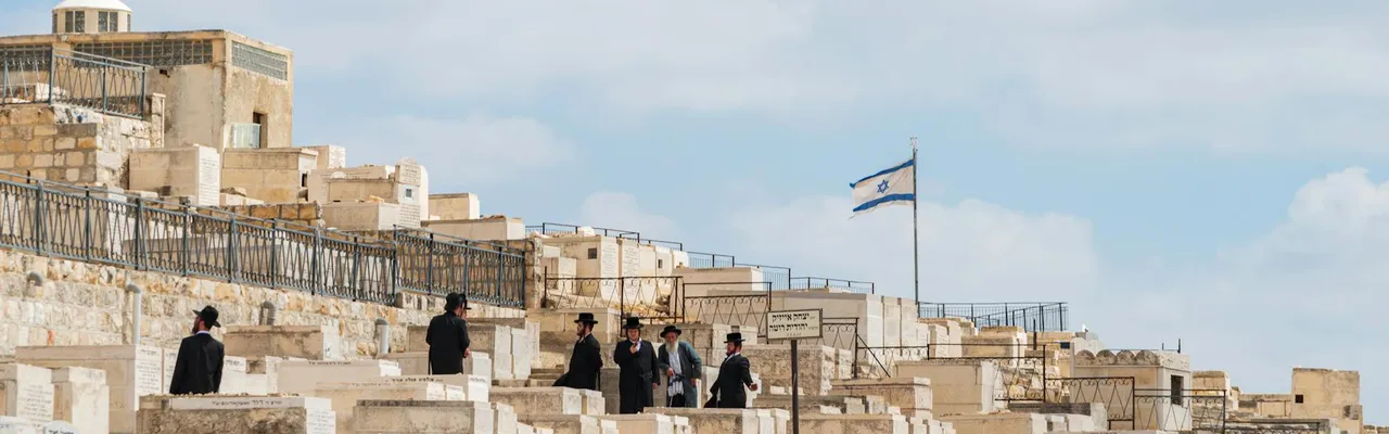 Orthodox Jewish men gather at Mount of Olives Cemetery in Jerusalem, Israel, under a clear sky.