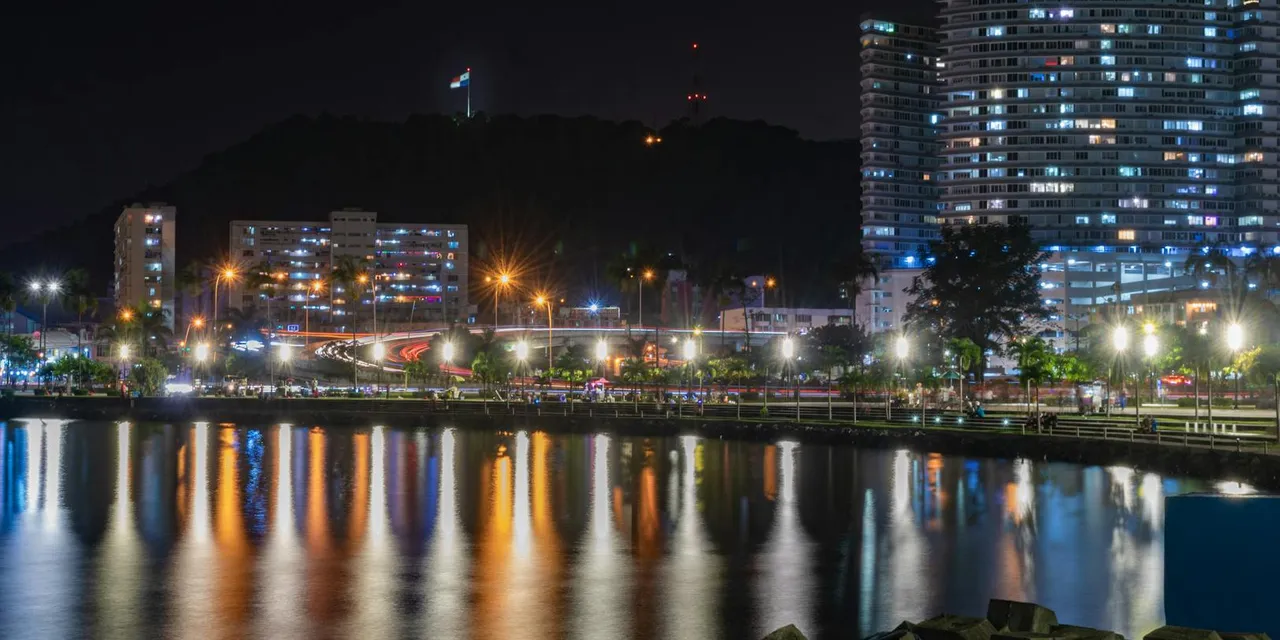 Illuminated Panama City skyline reflecting in calm harbor waters at night.