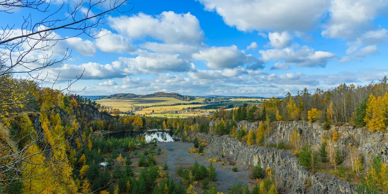 Beautiful aerial view of a quarry with autumn foliage and blue skies in Czechia.