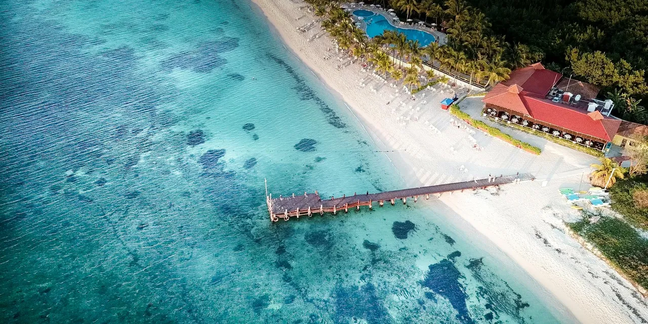 Aerial shot of a tropical beach with a pier, turquoise waters, and a resort in Cozumel.