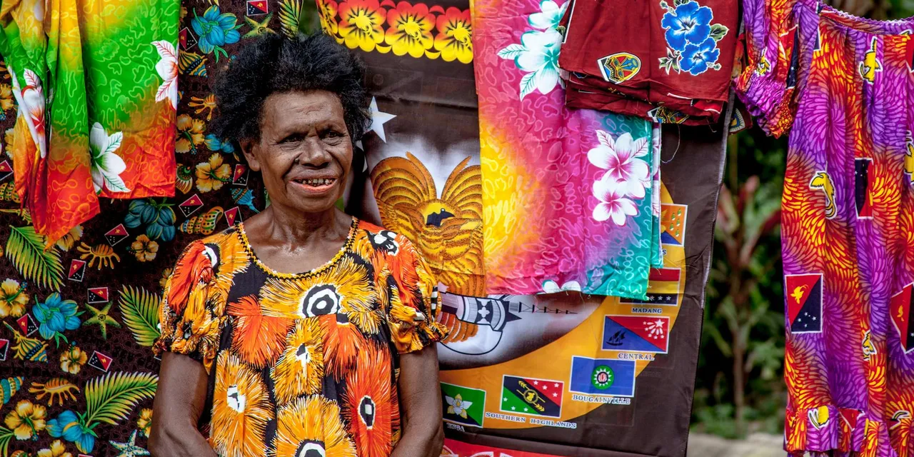 A senior woman stands smiling amidst vibrant traditional Papua New Guinean clothing.