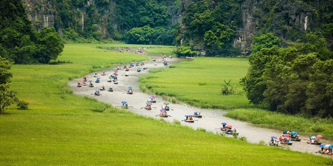 Crowd of people floating on river between grassy fields near green lush trees during trip in Vietnam in Tam Coc