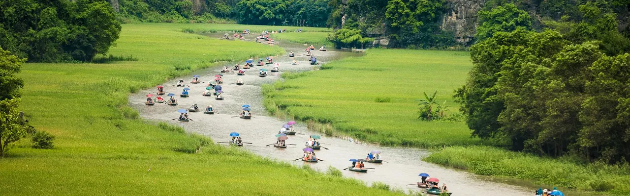 Crowd of people floating on river between grassy fields near green lush trees during trip in Vietnam in Tam Coc
