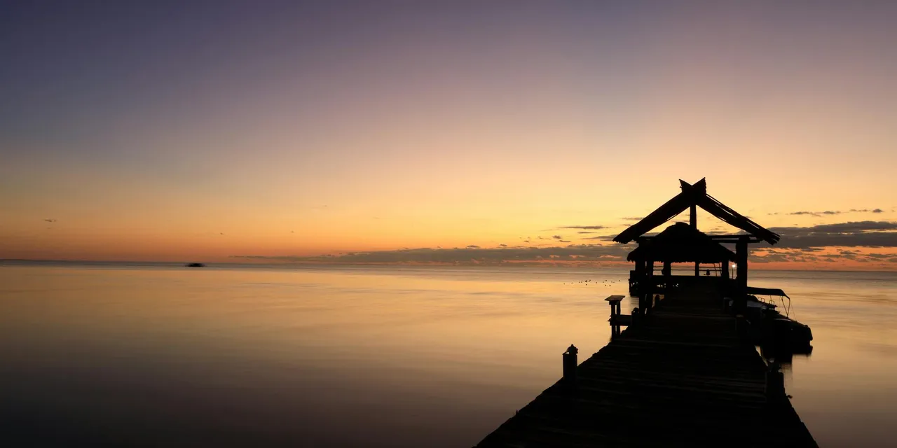 Tranquil sunset over a pier in San Pedro, Belize, capturing peaceful reflections and a dramatic sky.