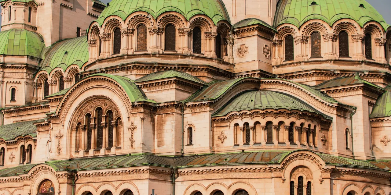 The green copper domes and pale stone facade of a neo-Byzantine cathedral in Sofia.