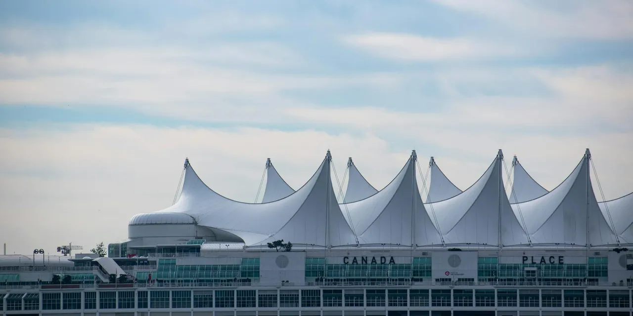 Iconic Canada Place building with its sail-like roof in Vancouver, BC against a blue sky.