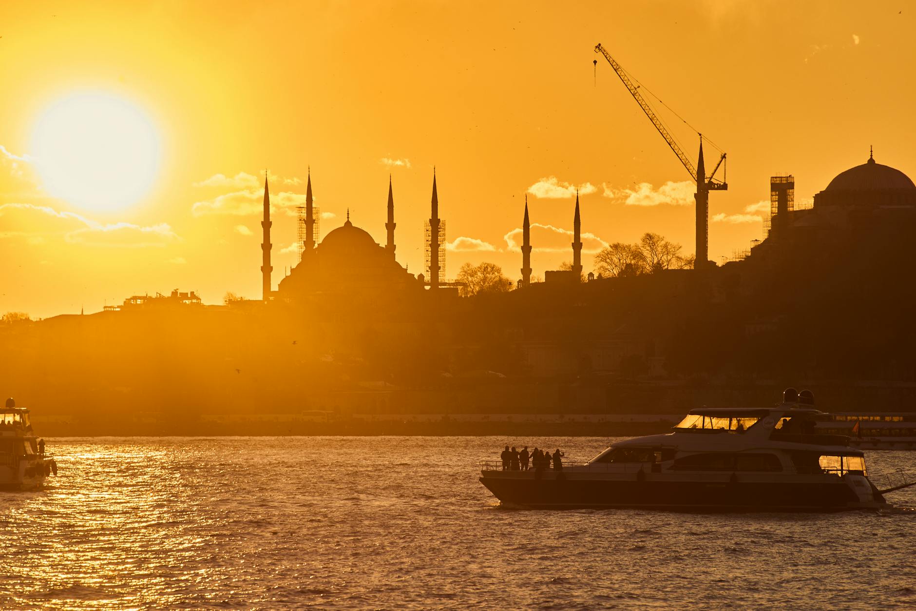 Silhouette of Istanbul mosques at sunset with vibrant golden hues and boats on the Bosphorus.