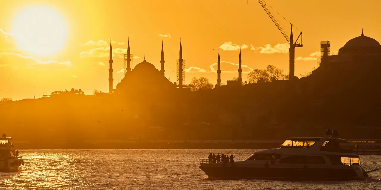 Silhouette of Istanbul mosques at sunset with vibrant golden hues and boats on the Bosphorus.