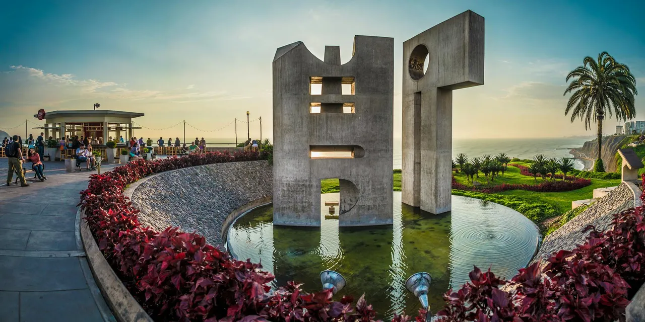 Modern concrete sculpture by the ocean in Lima, Peru with vibrant foliage and people enjoying the scene.