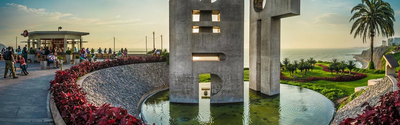 Modern concrete sculpture by the ocean in Lima, Peru with vibrant foliage and people enjoying the scene.