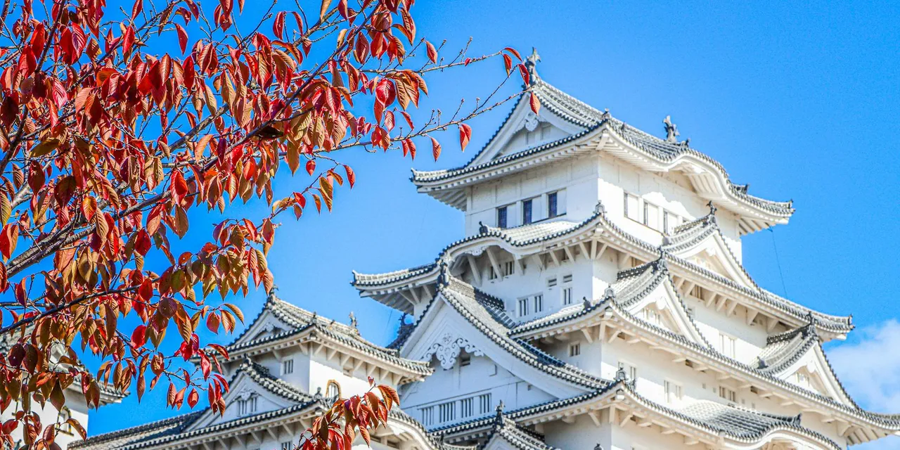 A stunning view of Himeji Castle with vibrant autumn leaves against a clear blue sky.
