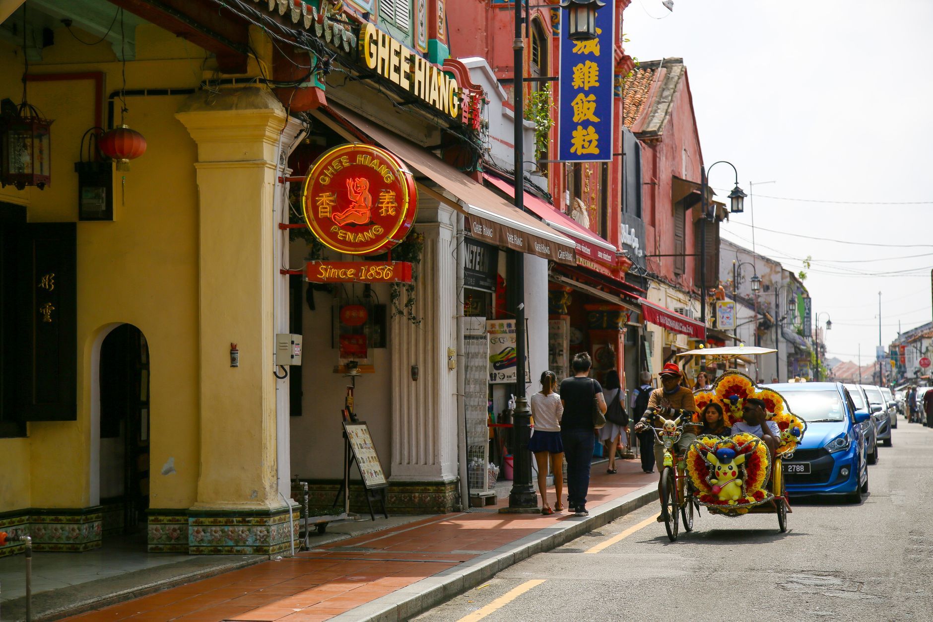 Vibrant trishaw passing traditional shops on a sunny Malacca street.