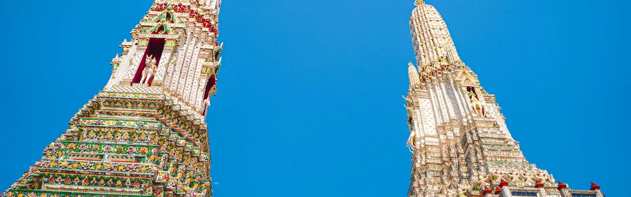 Low angle view of Wat Arun's ornate towers against a clear blue sky in Bangkok, Thailand.
