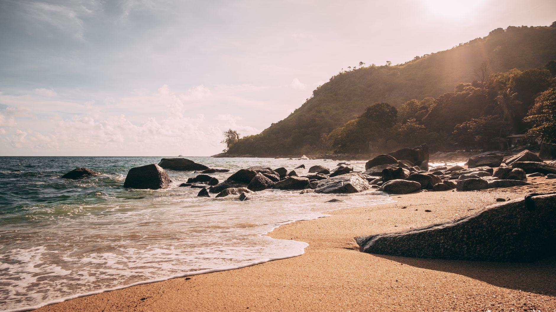 Dramatic sunset over a rocky shoreline in Phuket, Thailand, showcasing the serene beauty of a tropical beach.