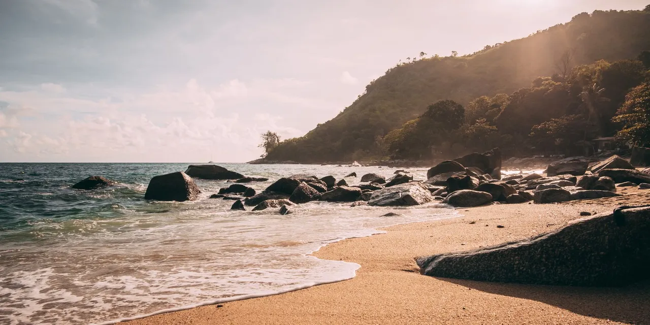Dramatic sunset over a rocky shoreline in Phuket, Thailand, showcasing the serene beauty of a tropical beach.