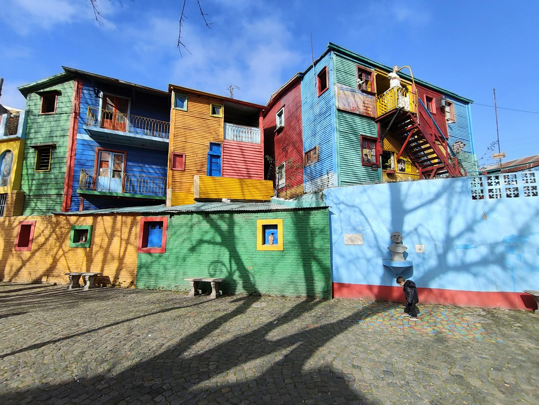 Vividly painted buildings in La Boca, Buenos Aires with shadows and street art.