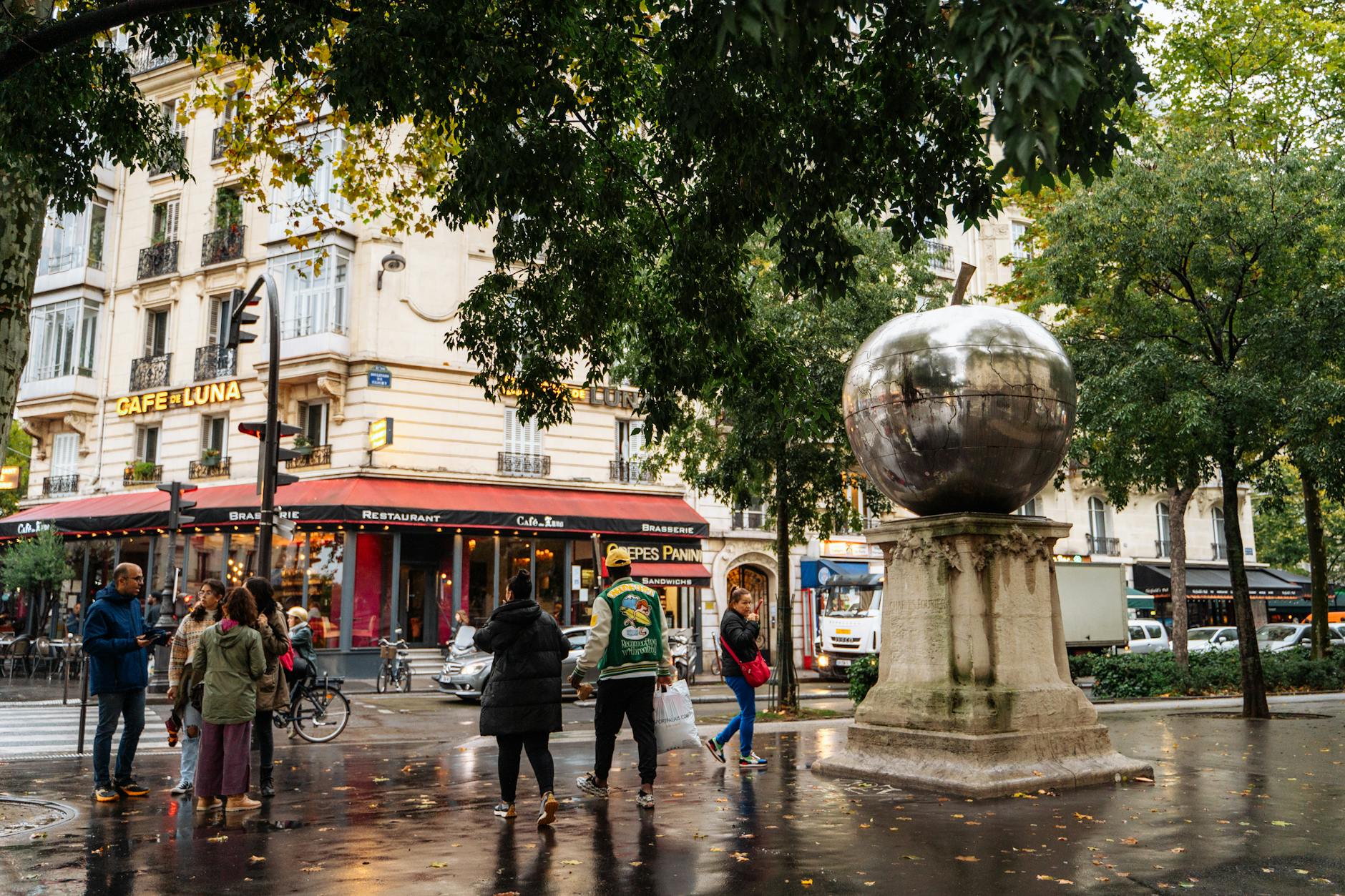 A vibrant Paris street scene featuring a cafe, sculpture, and people.